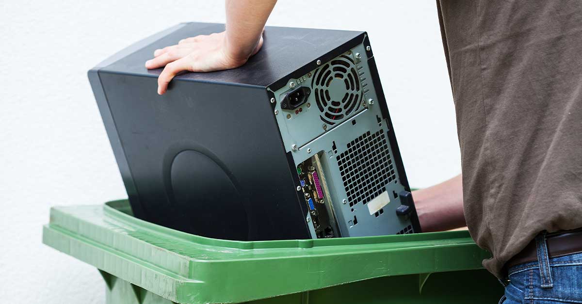 Person crams a desktop computer into a recycle bin