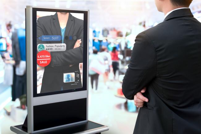 Man standing in front of an augmented reality mirror at a store showing the prices of the items he is trying on