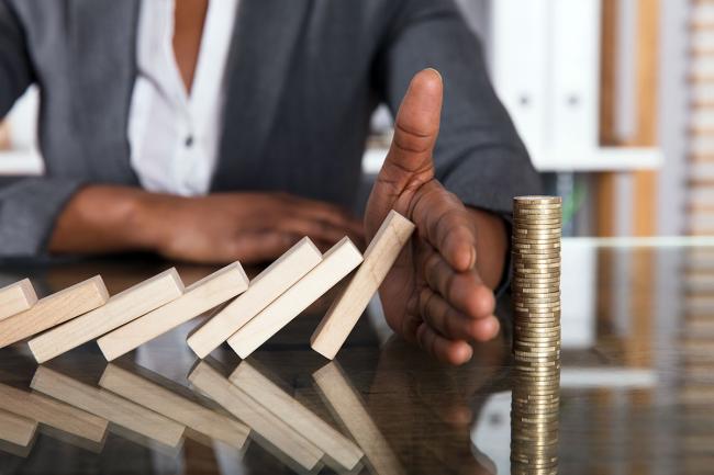 Businessperson hand blocks domino effect on tower of coins