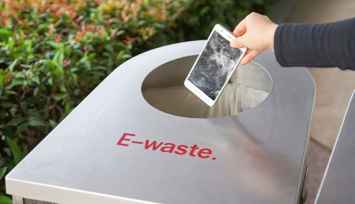 Hand drops a broken smartphone into an e-waste bin